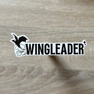 May include: A white sticker with a black silhouette of a bird with wings spread, flying above a cloud. The text "WINGLEADER" is printed in black letters below the bird.