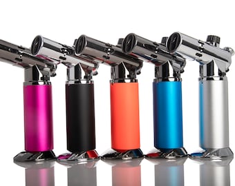 May include: Five butane torch lighters in different colors: pink, black, orange, blue, and silver. The lighters have a chrome finish and a long, narrow nozzle.