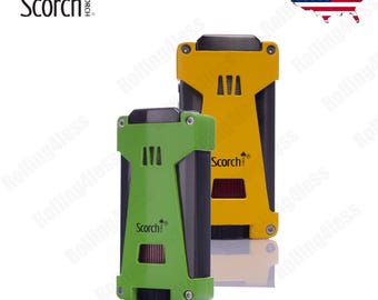 May include: Two Scorch brand lighters, one green and one yellow, with a black metal frame and a silver top. The lighters have a rectangular shape and a textured surface. The lighters are both labeled with the Scorch logo and the word "Torch".