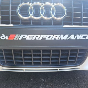 May include: A white Audi with a black grille and the text "Audi PERFORMANCE" on the front bumper.