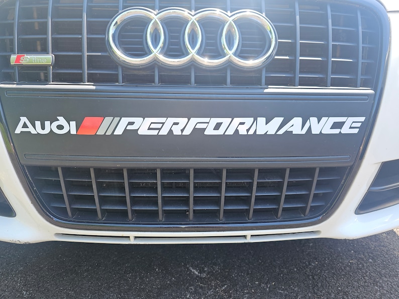 May include: A white Audi with a black grille and the text "Audi PERFORMANCE" on the front bumper.