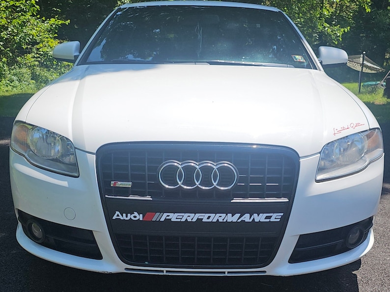 May include: White Audi sedan with a black grille and the words "Audi Performance" in red and black lettering.