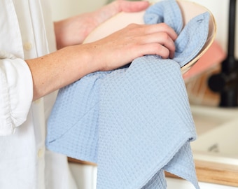 May include: A person is drying a light blue dish towel on a ceramic plate. The plate is light brown with a pink rim.