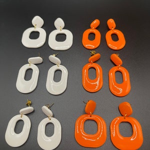 May include: A set of six pairs of earrings, three pairs are white and three pairs are orange. The earrings are all oval shaped with a hole in the center. The earrings are made of a smooth, glossy material.