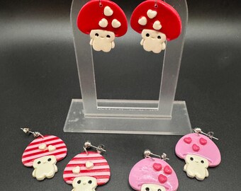 May include: Five pairs of handmade polymer clay mushroom earrings. Two pairs are red with white hearts, one pair is pink with white hearts, and two pairs are red and white striped.