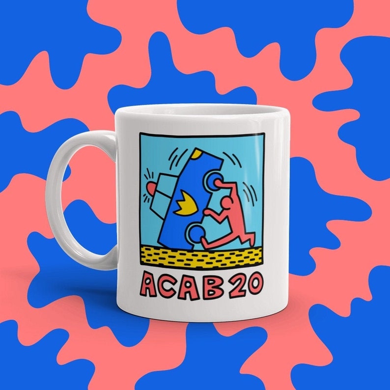 K&ouml;nnte beinhalten: Wei&szlig;e Keramiktasse mit einer blauen, gelben und roten Illustration einer Person, die ein blaues Auto schiebt. Der Text "ACAB 20" ist in Schwarz unter der Illustration gedruckt.