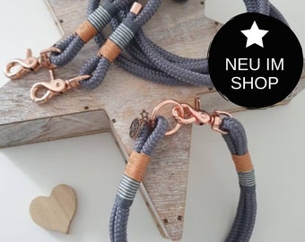 Puede incluir: Dos correas para perros de cuerda gris con herrajes de oro rosa y rayas blancas. Una correa es una correa de doble extremo con dos clips. La otra correa es un collar de bucle único con un clip. Las correas están sobre una superficie de madera en forma de estrella.