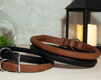 May include: Three leather dog collars, one brown and two black, with silver buckles. The collars are arranged on a wooden surface.