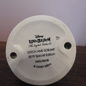 May include: White ceramic figurine base with black text that reads "Disney Lilo & Stitch The English Ladies Co Stitch and Scrump 2019 Special Edition England&reg; &copy; DISNEY 08819".
