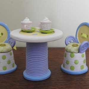 Peut inclure: Un ensemble de thé miniature fabriqué à partir de matériaux recyclés. L'ensemble comprend une table avec une base violette et bleue, deux chaises à pois jaunes et verts et deux tasses blanches avec un glaçage rose et blanc.