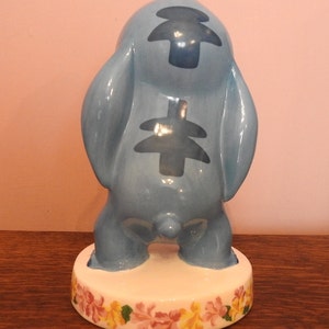 May include: A blue ceramic figurine of Stitch from Lilo & Stitch. The figurine is standing on a base with a floral design.
