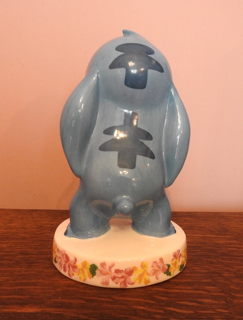 May include: A blue ceramic figurine of Stitch from Lilo & Stitch. The figurine is standing on a base with a floral design.