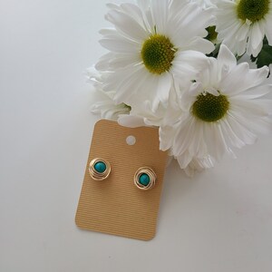 Peut inclure: Une paire de boucles d'oreilles en fil de fer doré avec des pierres turquoise. Les boucles d'oreilles sont présentées sur une carte marron.
