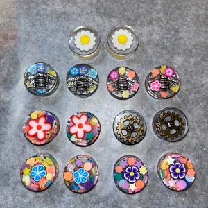 May include: Assortment of 12 colorful resin cabochons with various designs, including flowers, bees, and gears. The cabochons are set in clear resin and have a glossy finish.