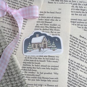 May include: A sticker featuring a snowy winter scene with a small house, trees, and a snowman. The sticker is on a page of a book with text about a baby.
