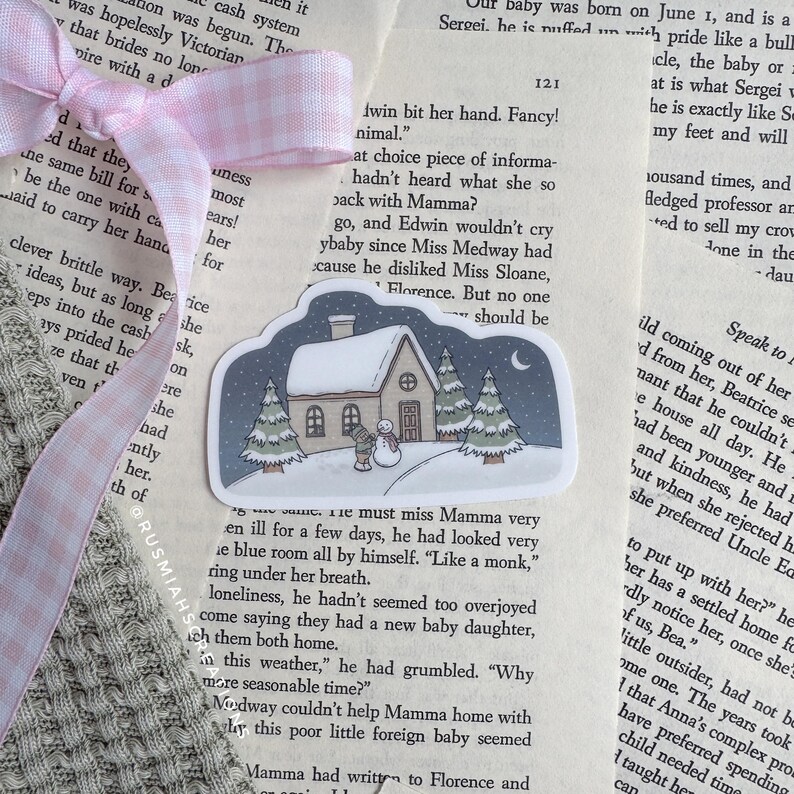 May include: A sticker featuring a snowy winter scene with a small house, trees, and a snowman. The sticker is on a page of a book with text about a baby.