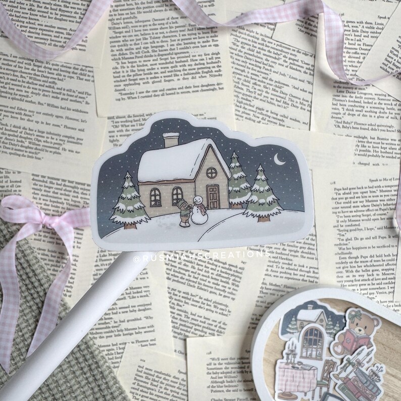 May include: A sticker featuring a winter scene with a small house, two pine trees, a snowman, and a person building the snowman. The sky is dark blue with a crescent moon and stars. The house has a white roof and a brown door. The sticker is on a white background.