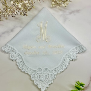 May include: White handkerchief with embroidered details. Features a large letter "M" and the names "Megan and Brandon" along with the date "October 25, 2025". The edges are trimmed with delicate lace.