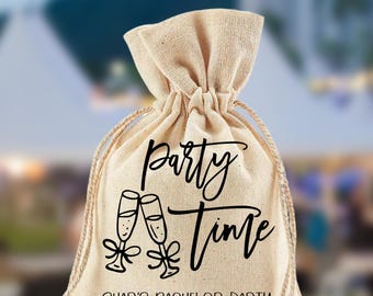 May include: A beige drawstring bag with the words "Party Time" in black script, along with two champagne flutes. The text "Shar's Bachelor Party Recovery Kit" is printed below. The bag is sitting on a wooden surface.