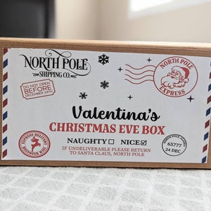 Könnte beinhalten: Eine braune Weihnachtsabend-Box aus Pappe mit einem weißen Etikett. Das Etikett trägt die Aufschrift "Valentina's CHRISTMAS EVE BOX" und enthält einen North Pole Express-Stempel, Schneeflocken und den Text "DO NOT OPEN BEFORE DECEMBER 24TH".