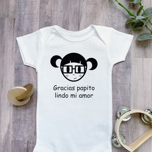May include: White baby onesie with a black cartoon girl wearing glasses and the text "Gracias papito lindo mi amor".