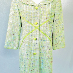 May include: A long-sleeved coat in a light green tweed fabric with a multicolored flecked pattern. The coat features a wide collar, four round lime green buttons down the front, and decorative lime green piping that crosses at the waist.