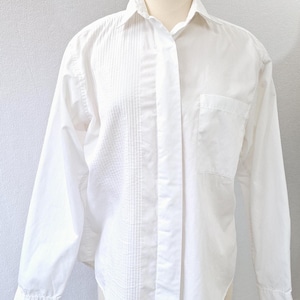 May include: A white long-sleeve button-down shirt with a pleated detail on the front. The shirt has a single chest pocket.