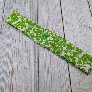 May include: A green and white patterned fabric headband with a green button.