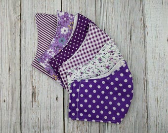 May include: A set of six purple fabric face masks with different patterns, including polka dots, stripes, and floral designs.