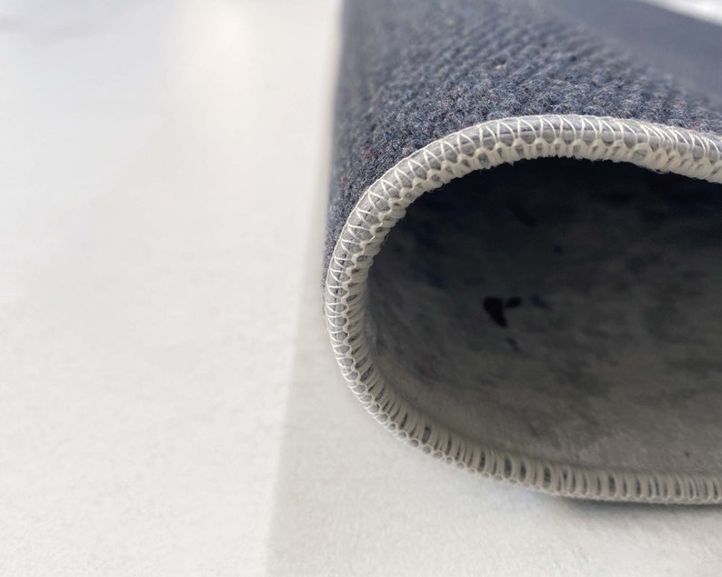 Puede incluir: Primer plano del borde de una alfombra gris oscuro con un borde blanco cosido.