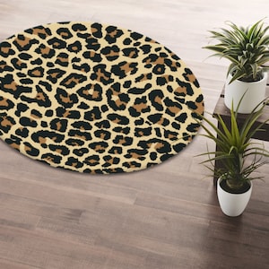 May include: A round, beige and brown rug with a leopard print pattern. The rug is on a wooden floor.
