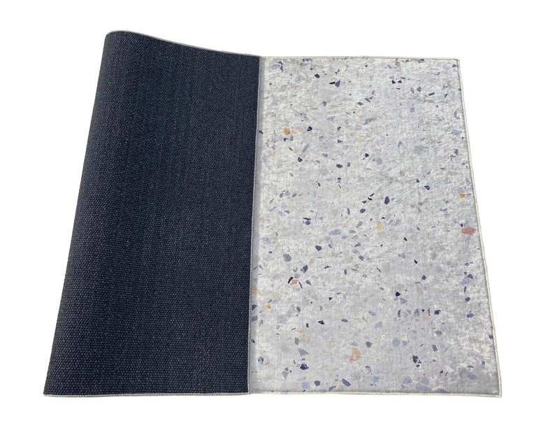 Puede incluir: Una esterilla de yoga reversible con un lado negro y un lado blanco con un patr&oacute;n moteado.