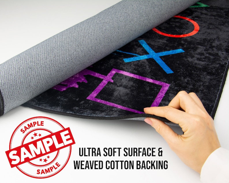 May include: A black and gray rug with colorful PlayStation controller symbols. The rug has a soft surface and a woven cotton backing. The text "SAMPLE" is printed on a red circle.