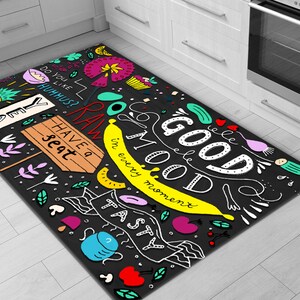 May include: A black and white kitchen rug with colorful illustrations of food and the text "Good Mood in every moment". The rug has a fun and whimsical design with a variety of fruits, vegetables, and other food items.