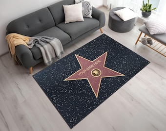 May include: A rectangular rug with a dark blue background and a large, red star in the center. The star has a gold border and the text "YOUR NAME HERE". The rug has a speckled pattern.