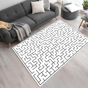 May include: A rectangular rug with a black maze pattern on a white background. The rug is placed on a light-colored wooden floor. The rug is a home decor item.