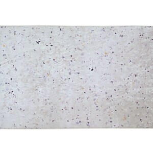 Puede incluir: Una alfombra blanca con un patr&oacute;n moteado de peque&ntilde;as motas de color marr&oacute;n claro, gris y negro. La alfombra tiene una superficie sutilmente texturizada.