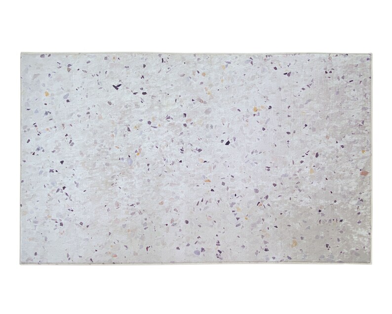 Puede incluir: Una alfombra blanca con un patr&oacute;n moteado de peque&ntilde;as motas de color marr&oacute;n claro, gris y negro. La alfombra tiene una superficie sutilmente texturizada.