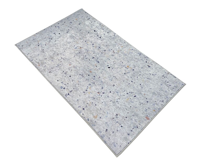 Puede incluir: Una alfombra blanca con un patr&oacute;n moteado de peque&ntilde;as motas grises claras, azules y naranjas.