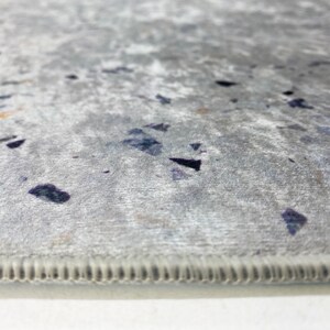 Puede incluir: Primer plano de una alfombra gris con un sutil patr&oacute;n moteado. La alfombra tiene un borde cosido.