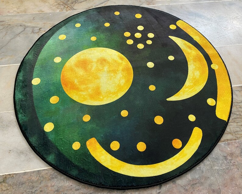 Pode incluir: Um tapete redondo com fundo verde escuro e uma lua amarela, uma lua crescente e outras formas. O tapete tem um brilho sutil.