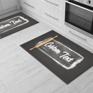 May include: Two gray kitchen rugs with a rolling pin and flour design. The text "Custom Text" is written on each rug.