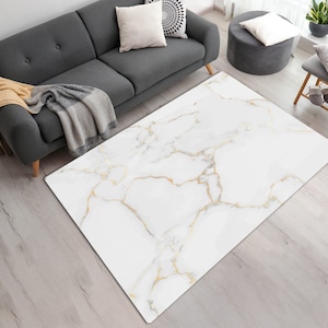 Könnte beinhalten: Weißer und goldfarbener Marmor-Teppich mit dezentem Muster. Der Teppich hat ein modernes Design und würde in einem Wohnzimmer oder Schlafzimmer gut aussehen.