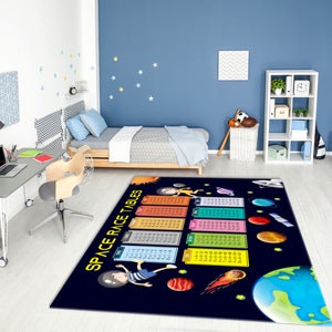 May include: A colorful rug with a space theme. It features a cartoon astronaut, planets, stars, and a table of multiplication facts. The rug is on a light wood floor in a room with a desk, chair, and bed.