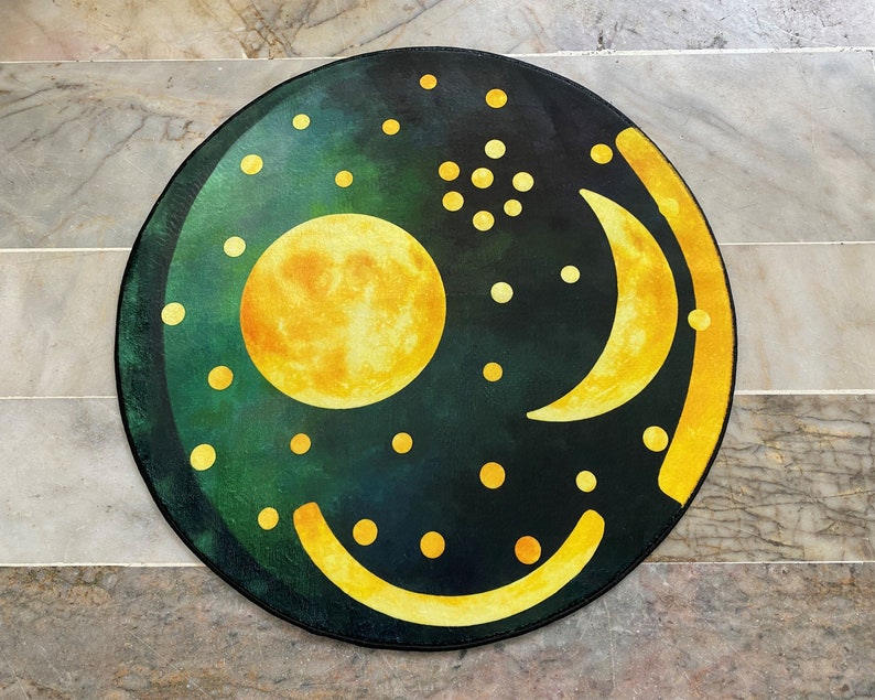 Pode incluir: Um tapete redondo verde e amarelo com um desenho de lua crescente e sol. O tapete tem um fundo verde escuro com pontos amarelos e uma lua crescente e um sol amarelos.