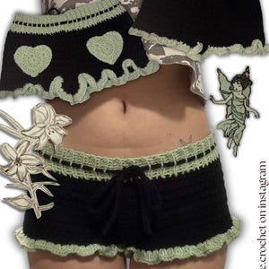 K&ouml;nnte beinhalten: Schwarze H&auml;kelshorts mit hellgr&uuml;ner Bord&uuml;re und Kordelzug. Die Shorts haben einen ger&uuml;schten Saum und ein Herzdesign. Das Bild zeigt auch einen passenden Rock mit Herzdesign und hellgr&uuml;ner Bord&uuml;re. Der Text "paige.crochet on instagram" ist sichtbar.