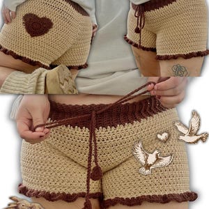 K&ouml;nnte beinhalten: Geh&auml;kelte Shorts in Beige und Braun mit einem braunen Herzdetail. Die Shorts haben einen Kordelzug in der Taille und einen R&uuml;schensaum. Bund und Saum sind dunkelbraun. Handgefertigt.