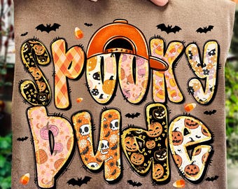 May include: A brown t-shirt with the words "Spooky Dude" in a colorful, Halloween-themed design. The text features pumpkins, bats, and candy corn accents. An orange baseball cap is incorporated into the design.