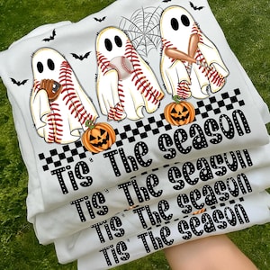 Puede incluir: Varias camisetas blancas apiladas con diseños de fantasmas con temática de béisbol. Cada fantasma sostiene una pelota, un bate o un guante de béisbol. También se imprimen calabazas de Halloween naranjas y el texto "Tis The season".