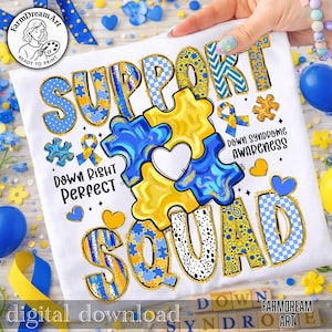 Op de afbeelding: Wit t-shirt met een kleurrijk grafisch ontwerp. Het ontwerp bevat de woorden "SUPPORT SQUAD" in blauw en geel, puzzelstukjes, harten en de zinnen "Down Right Perfect" en "Down Syndrome Awareness".
